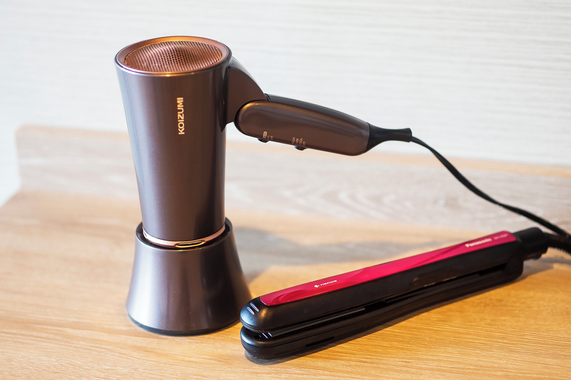 A hair straightener and a cylindrical device on a wooden surface.