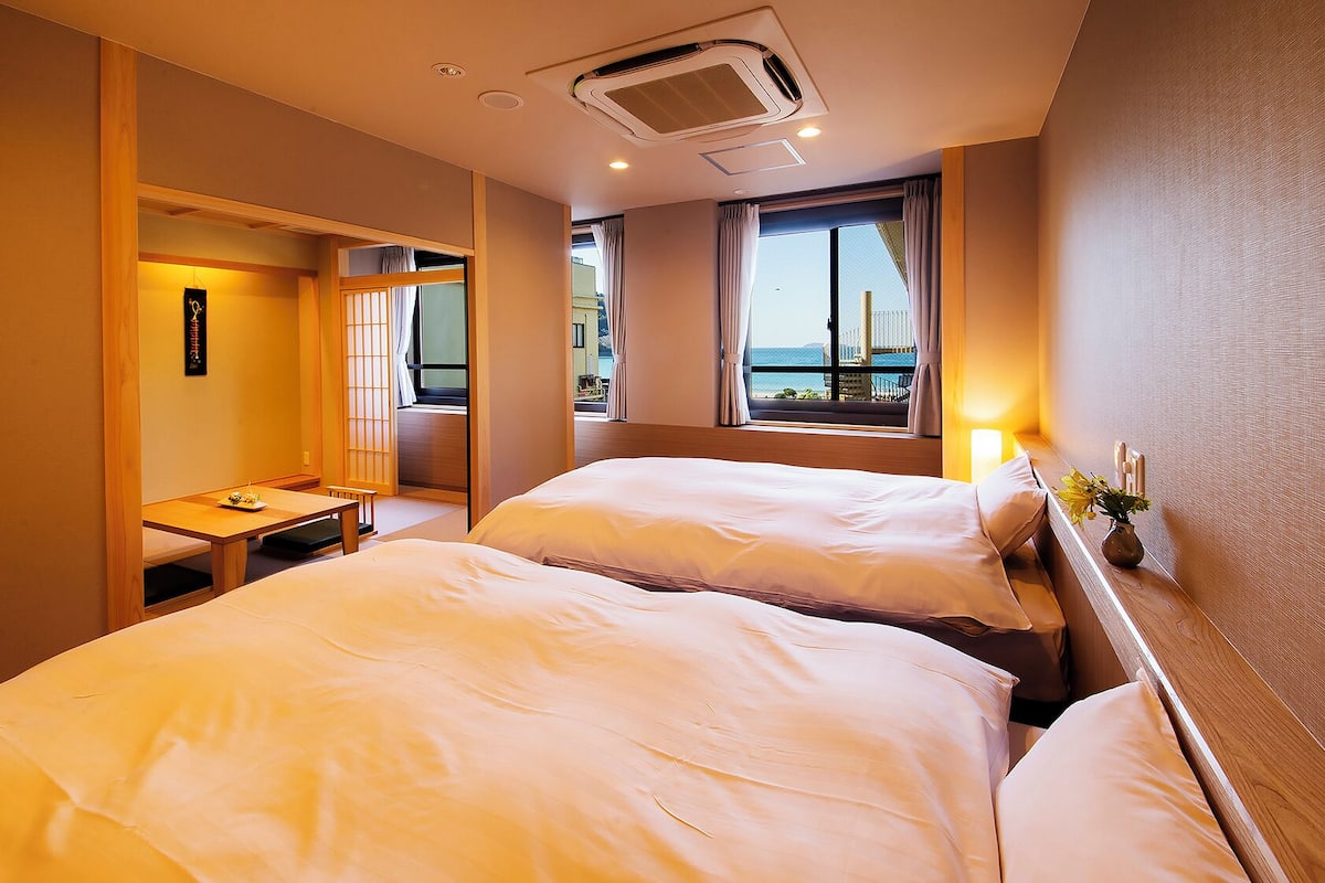 Habitación de hotel con dos camas, una mesita y vista al mar.