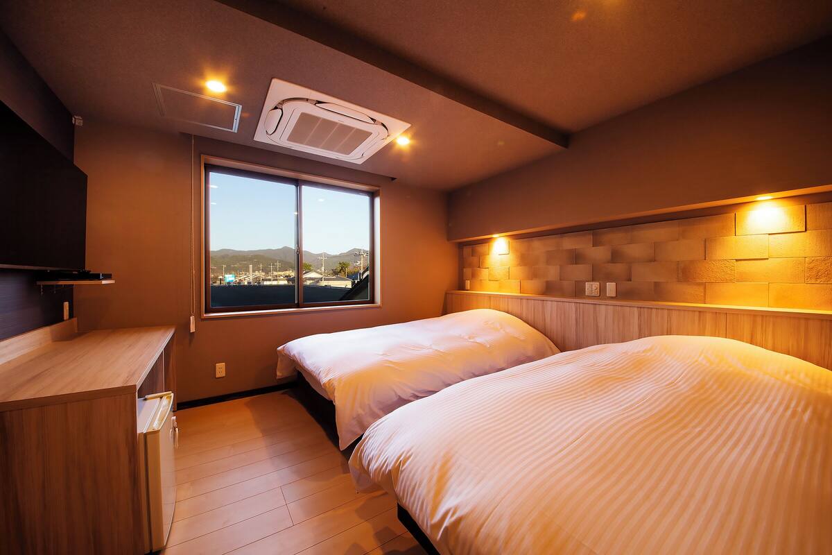 A bedroom with two beds, a window with a view, a wooden headboard, and a built-in wardrobe.