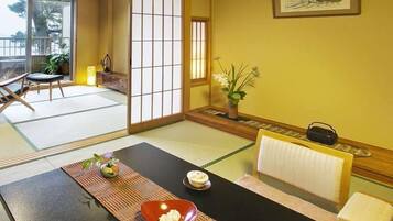 Ett traditionellt japanskt rum med tatamimattor på golvet, ett lågt bord med en röd skål, en liten vas med blommor och en inramad tavla på väggen.