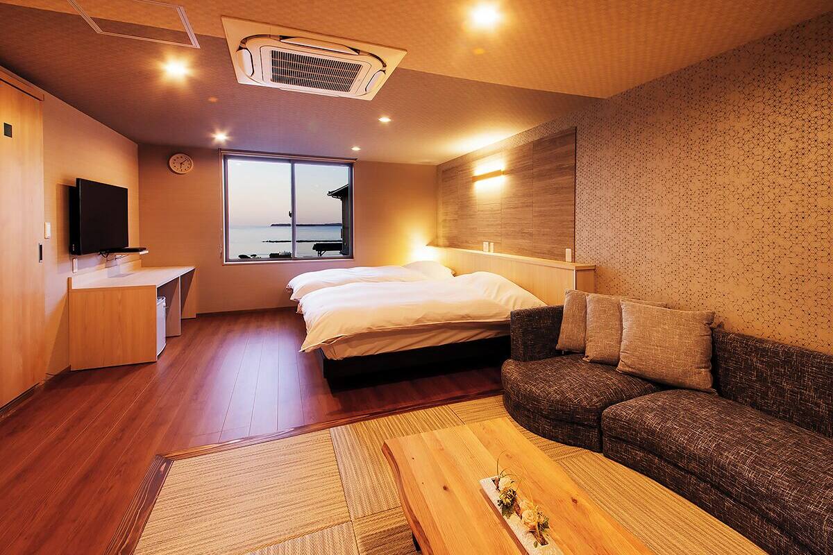 A hotel room with a bed, a sofa, a TV, a desk, and a large window with a view.