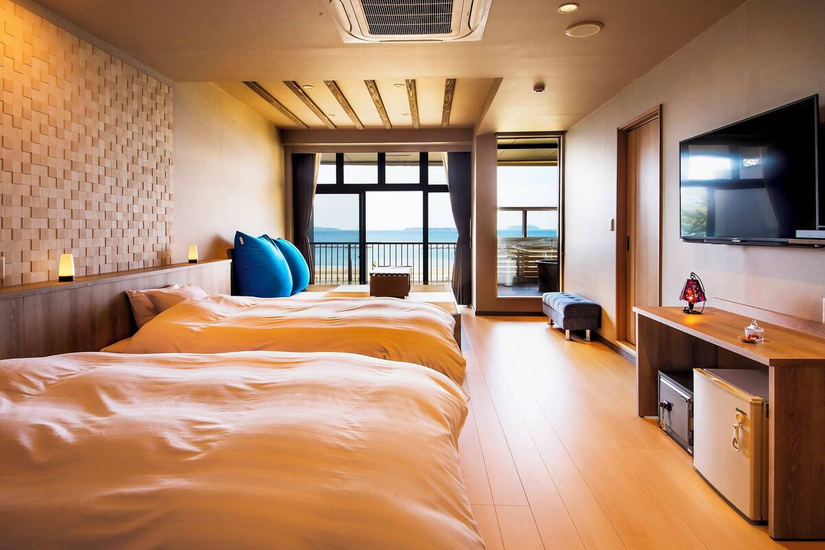 A hotel room with a large bed, a TV, a desk with a lamp, and a view of the sea.
