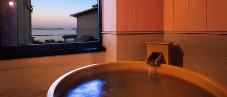 A hot tub with a view of the sea through a window.