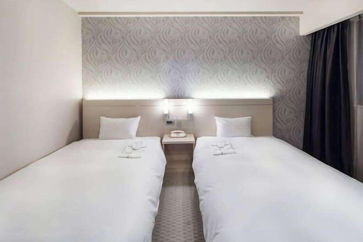 Une chambre d’hôtel avec deux lits simples, une table de chevet avec une lampe et un mur décoré d’un motif.