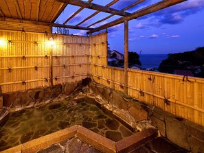 A traditional Japanese onsen with a stone hot spring, bamboo walls, and a view of the sea.