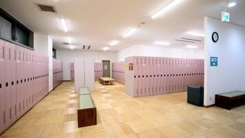 A locker room with multiple lockers, a wooden bench, and a trash bin.