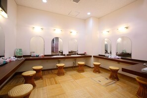 Un baño de hotel con varios espejos, un mostrador de recepción y taburetes de mimbre.