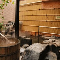 Un onsen japonés tradicional con tinaja de madera, asientos de piedra y pared de bambú.