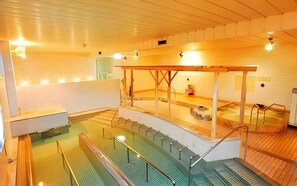 An indoor swimming pool with a wooden deck area, a hot tub, and a viewing platform.