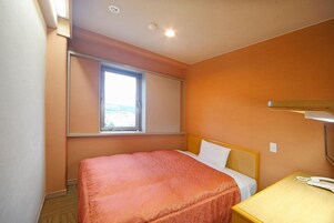 Una habitación de hotel con una cama individual, una mesita de noche con lámpara y una ventana con persianas.