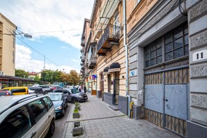 Une vue de rue avec des voitures garées, un immeuble doté d’un balcon et un portail fermé.