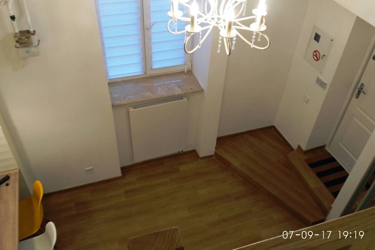 Une pièce avec un lustre, une fenêtre avec des stores, un radiateur et une porte sur laquelle est apposé un panneau «interdiction de fumer».