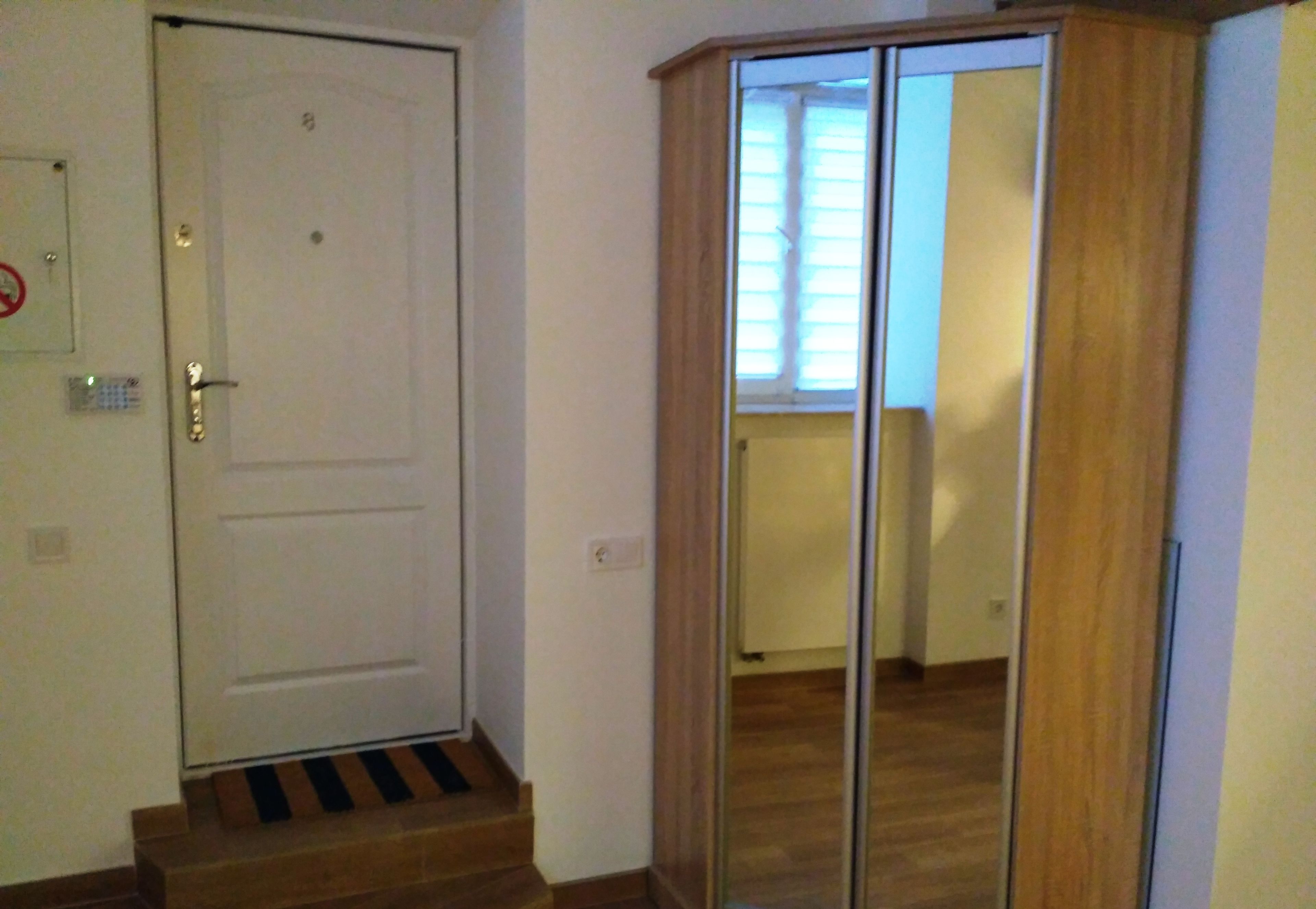 Une pièce avec une porte blanche, une armoire en bois et une fenêtre avec des stores.