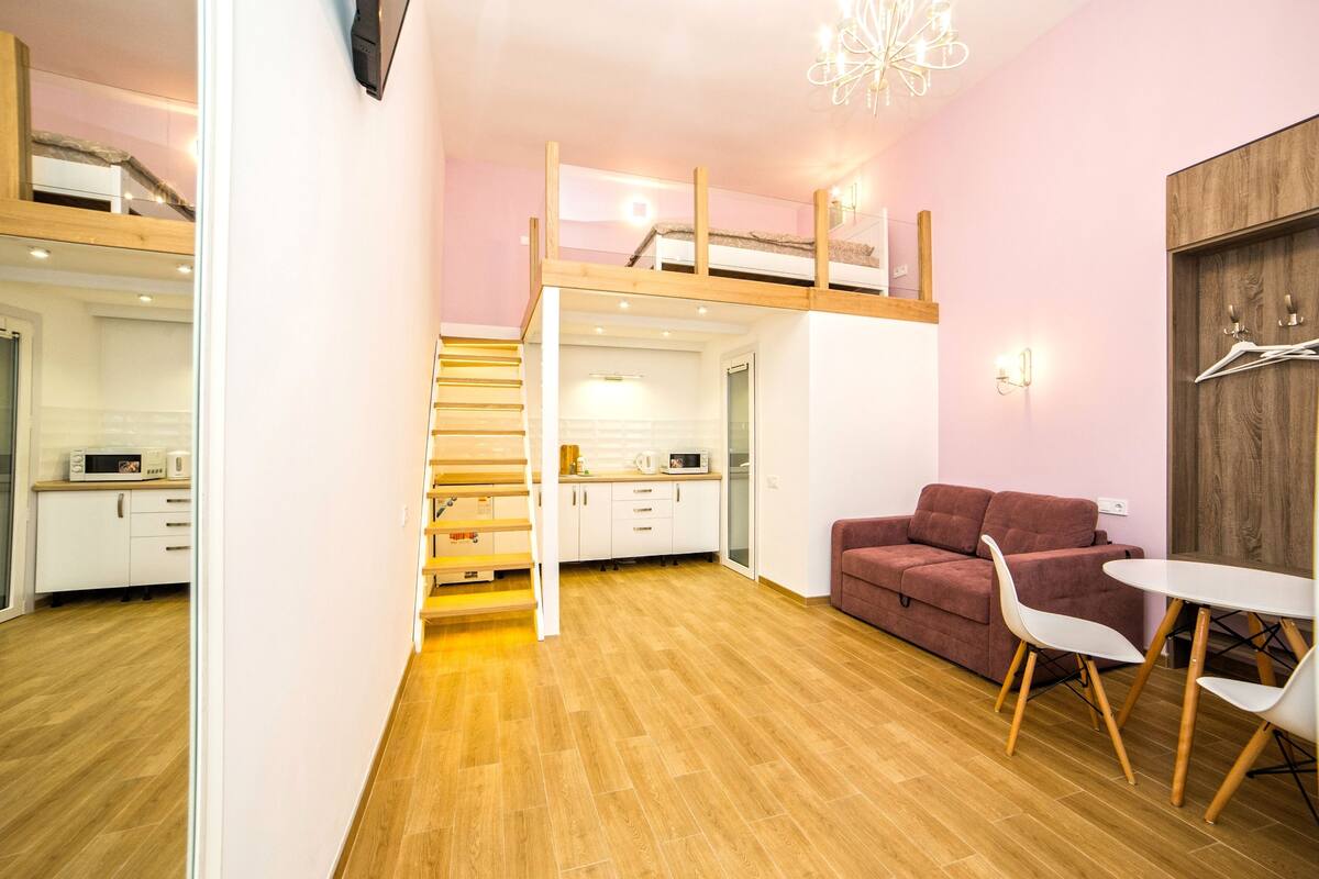 Un espace de vie compact comprenant un coin cuisine, un canapé, une table à manger et un escalier menant à un niveau supérieur.
