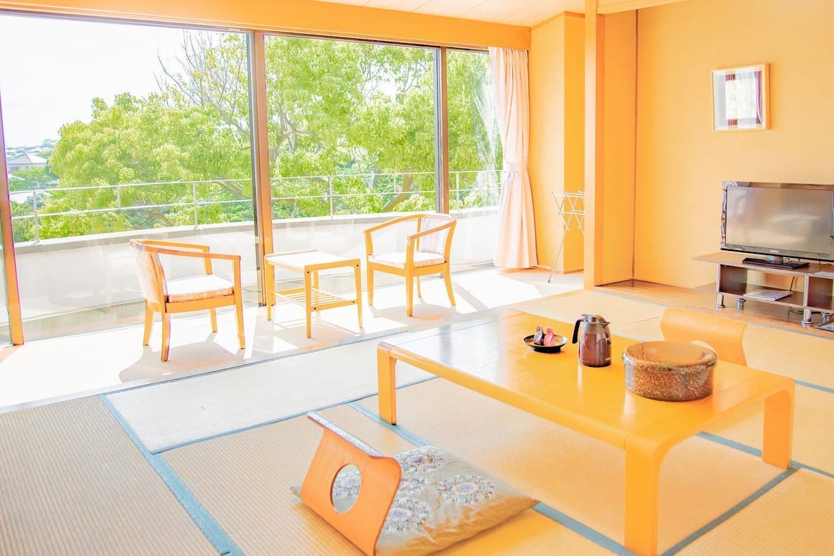 A modern living room with tatami flooring, a TV, and a balcony with a view.