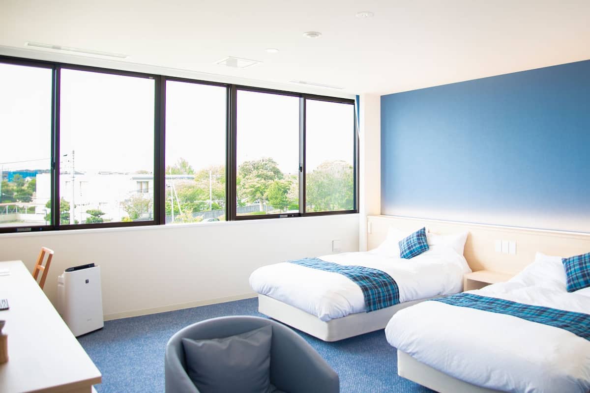 A hotel room with two beds, a desk, and a chair.