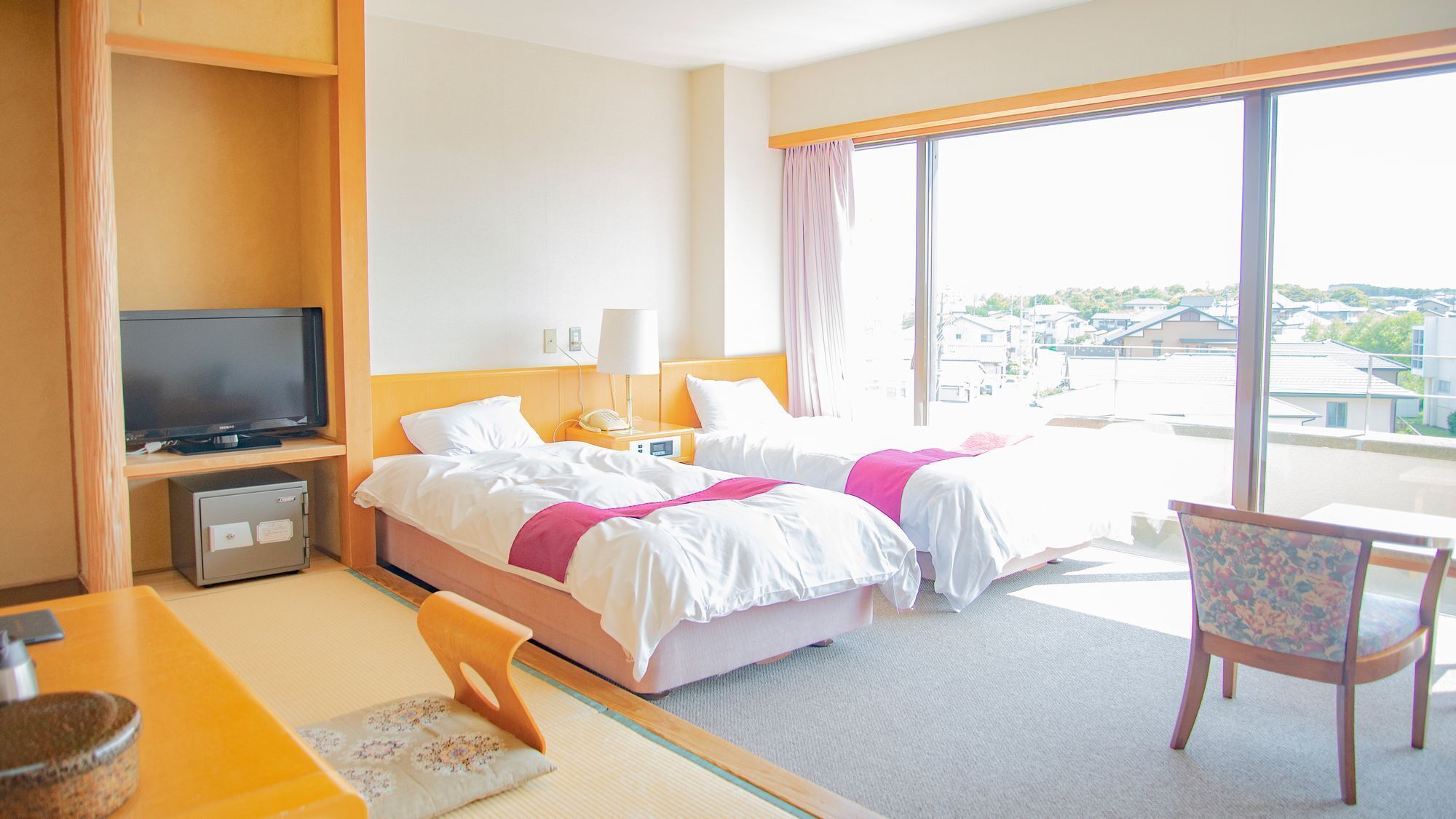 A hotel room with a bed, a TV, a desk, a chair, and a large window.