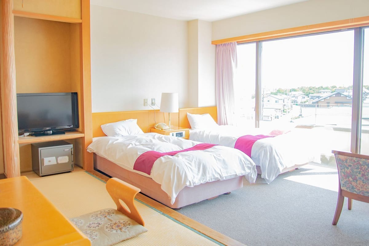 A hotel room with a bed, a TV, a desk, a chair, and a large window.