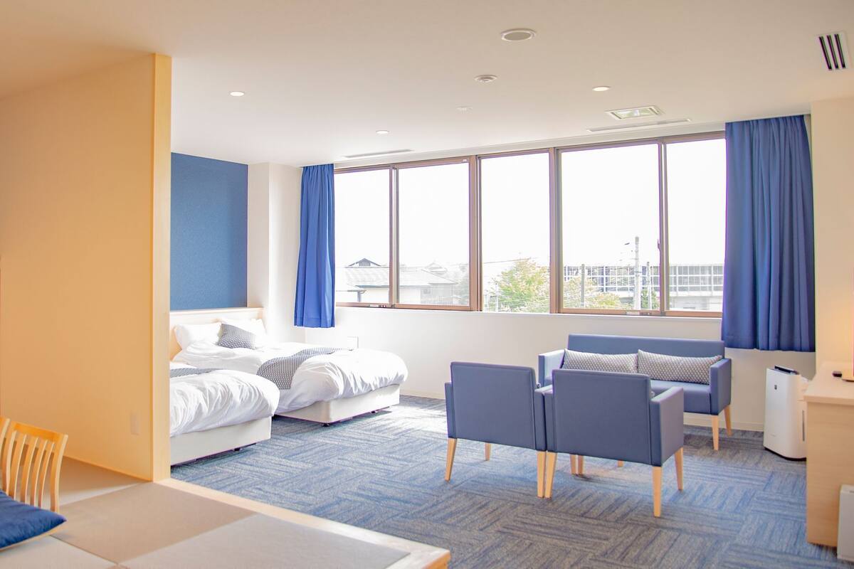 A modern hotel room with a bed, seating area, and large windows.