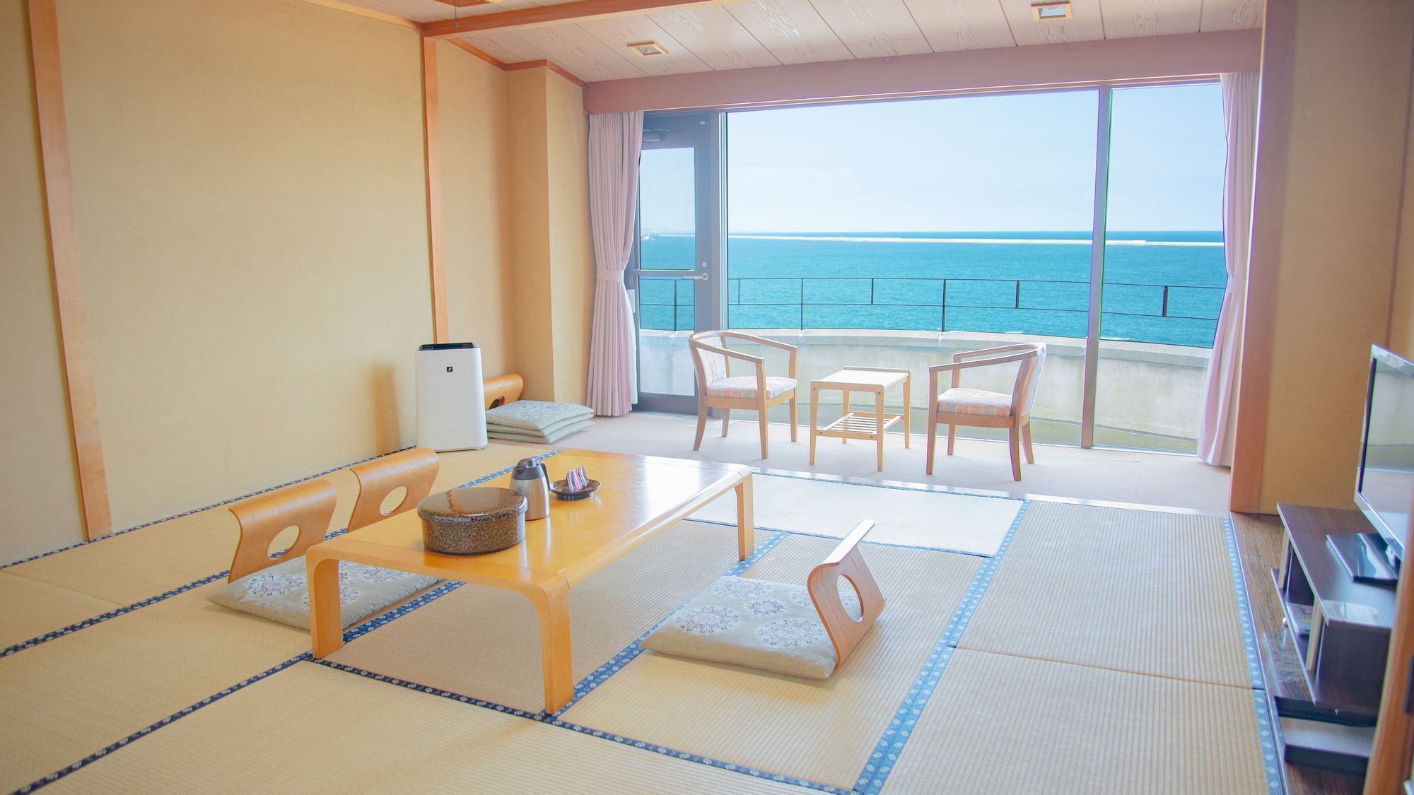 A room with tatami flooring, a low table with cushions, a TV, and a view of the sea.