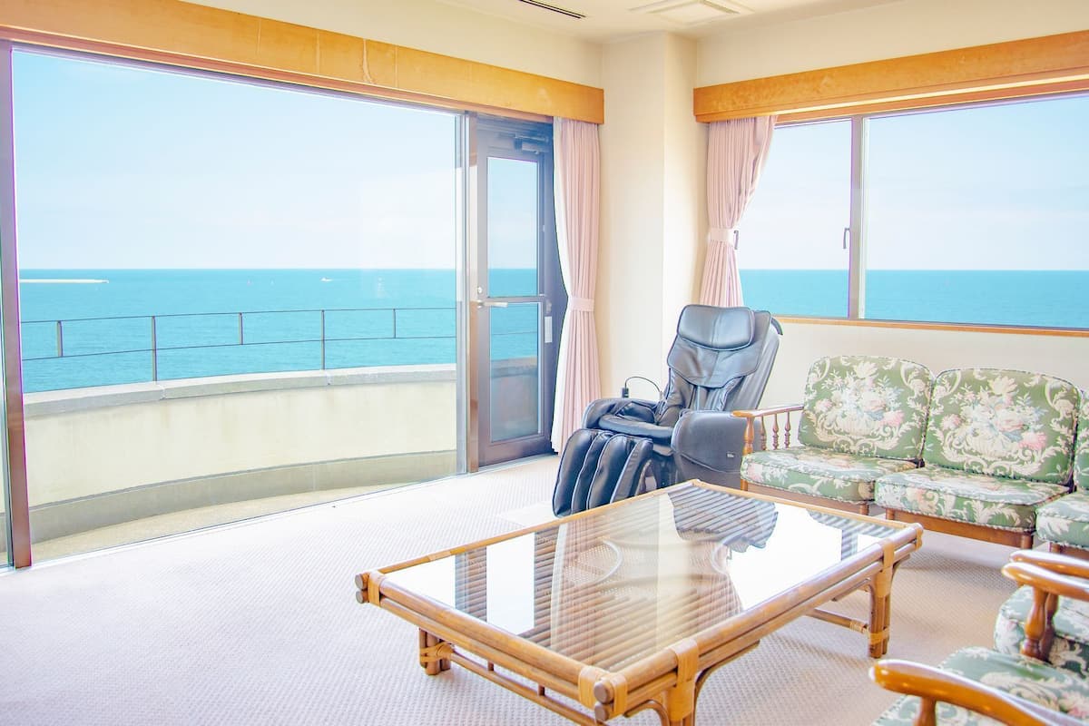 A balcony with a view of the sea, a massage chair, a sofa, and a table.