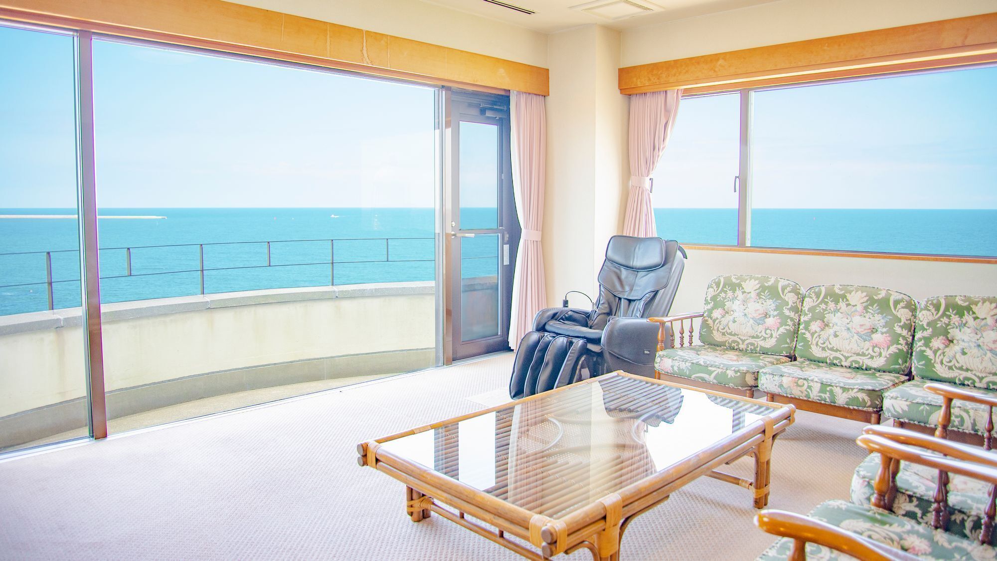 A balcony with a view of the sea, a massage chair, a sofa, and a table.