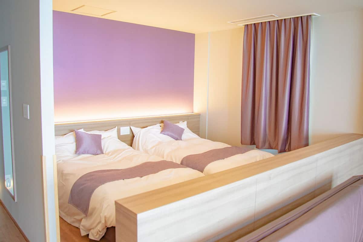 A double bed with a wooden headboard, a bedside table, and a window with curtains.