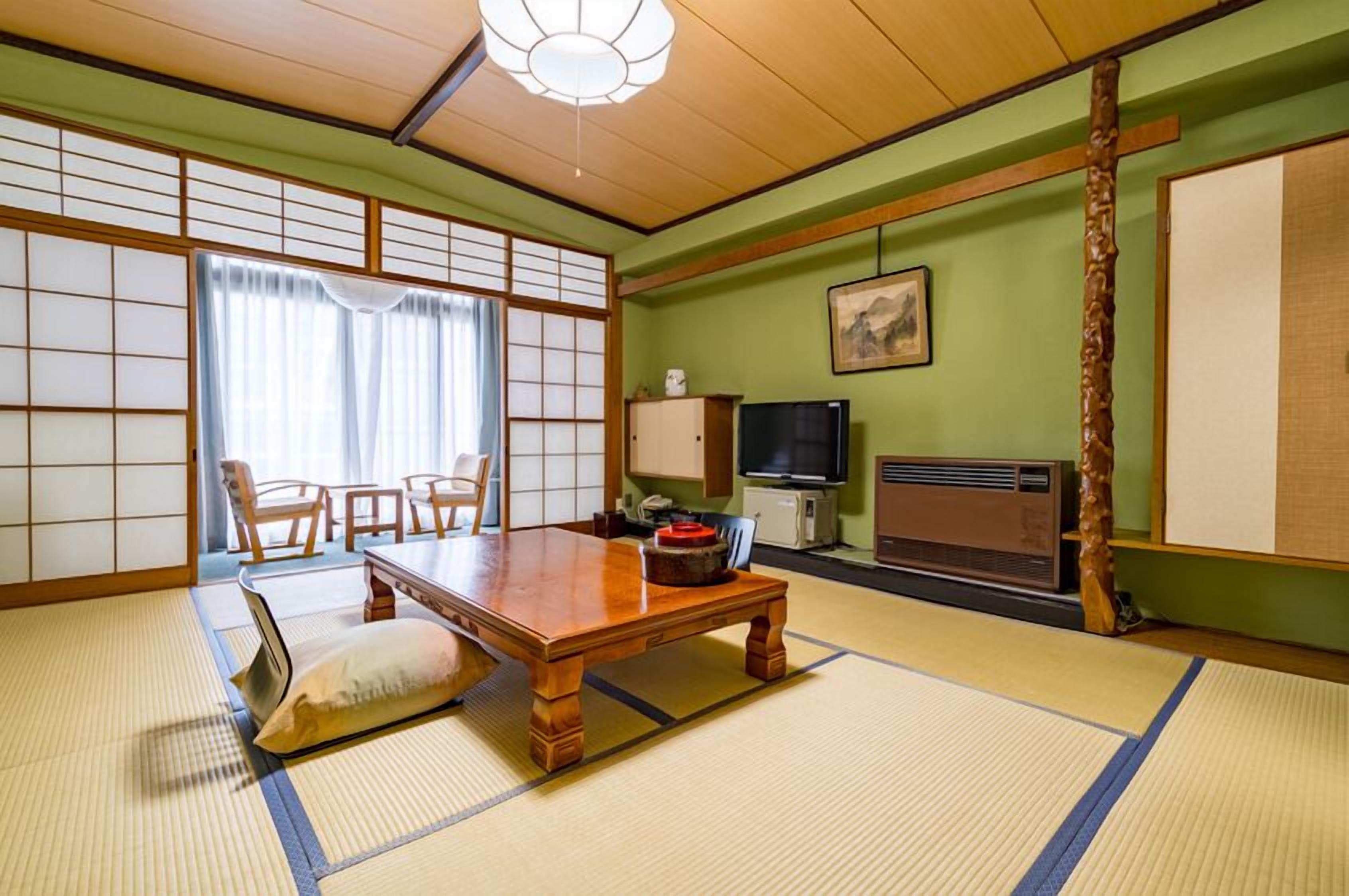 A traditional Japanese room with tatami flooring, a low wooden table, a television, and a cabinet.