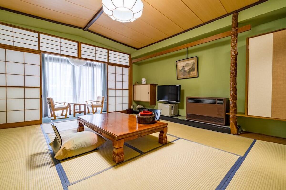 A traditional Japanese room with tatami flooring, a low wooden table, a television, and a cabinet.