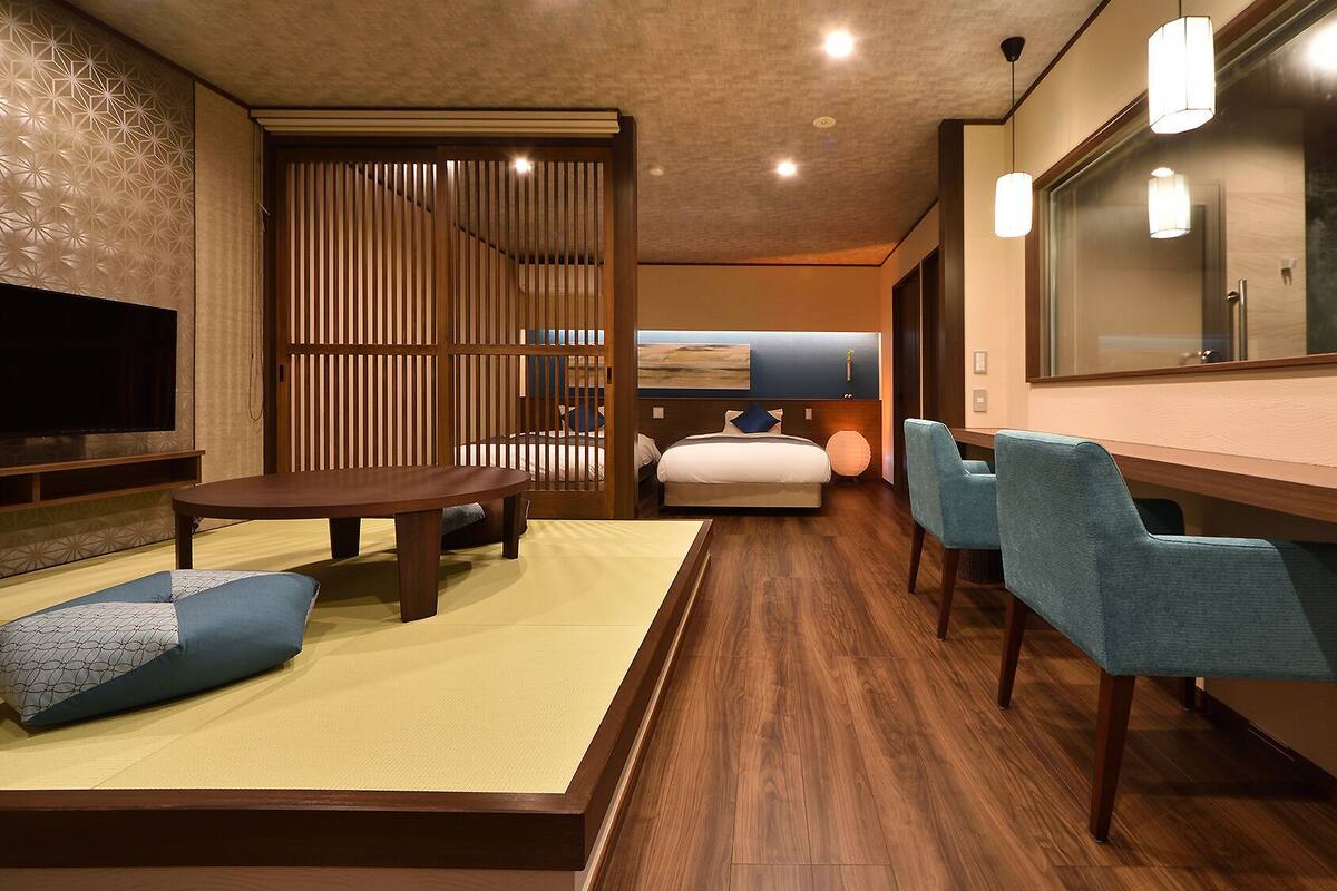 A modern hotel room with a wooden floor, a sofa, a dining table, and a TV.