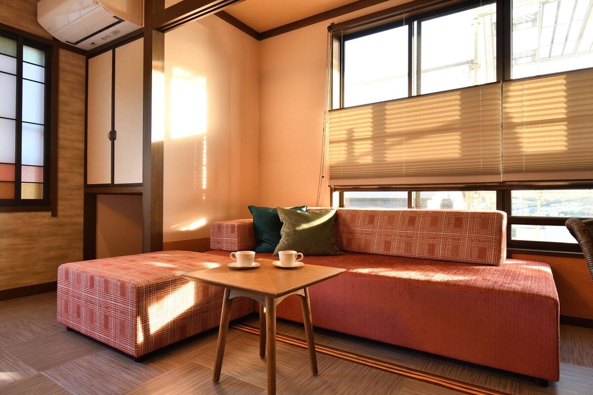 A room with a sofa, a table with cups, a window with blinds, and a traditional sliding door.