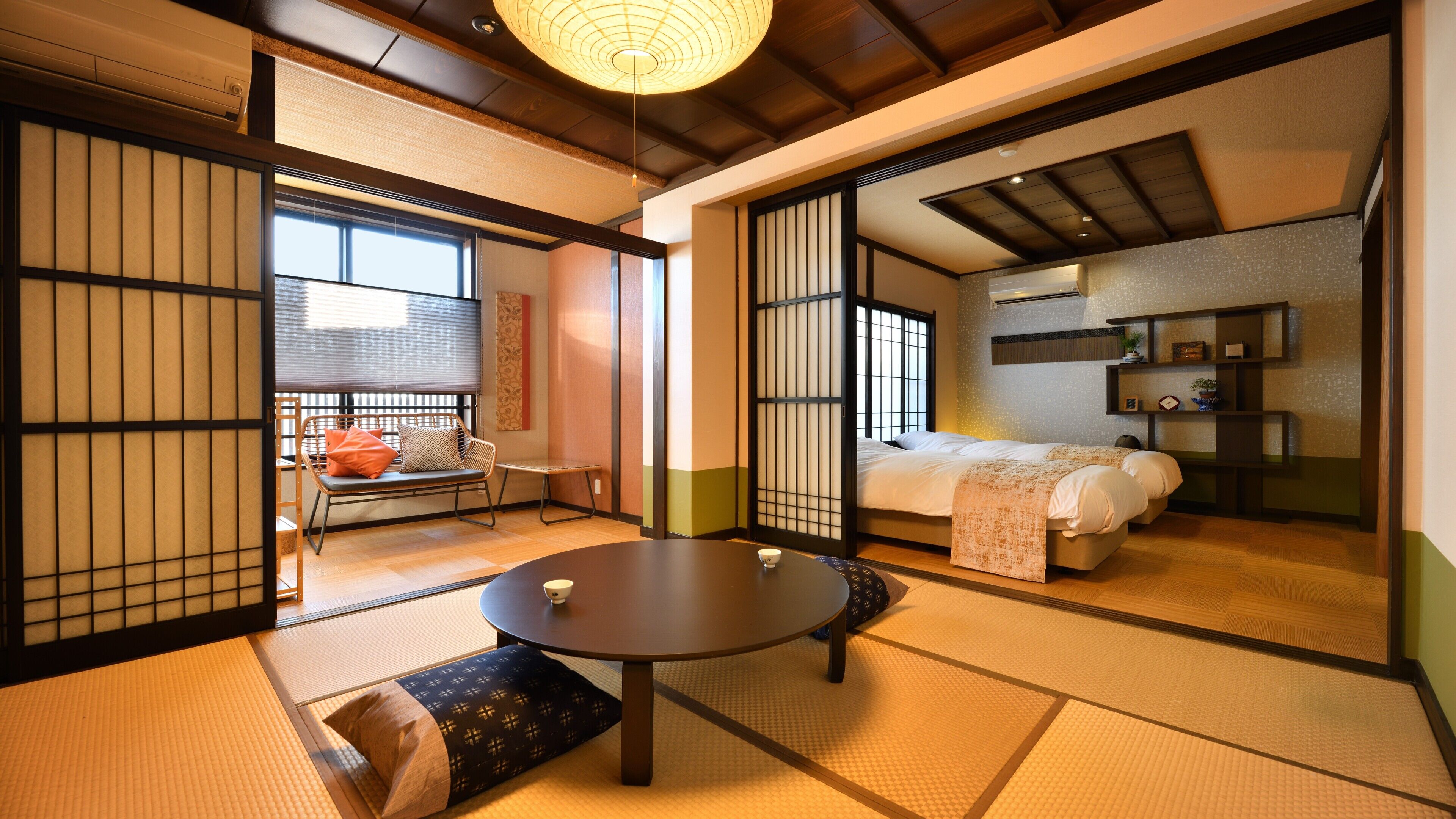 Um quarto japonês tradicional com tatames, uma mesa baixa, um sofá e uma cama com futon.