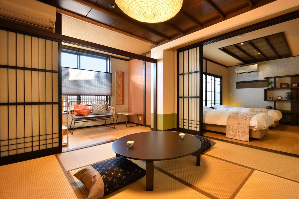 A traditional Japanese room with tatami flooring, a low table, a sofa, and a bed with a futon.