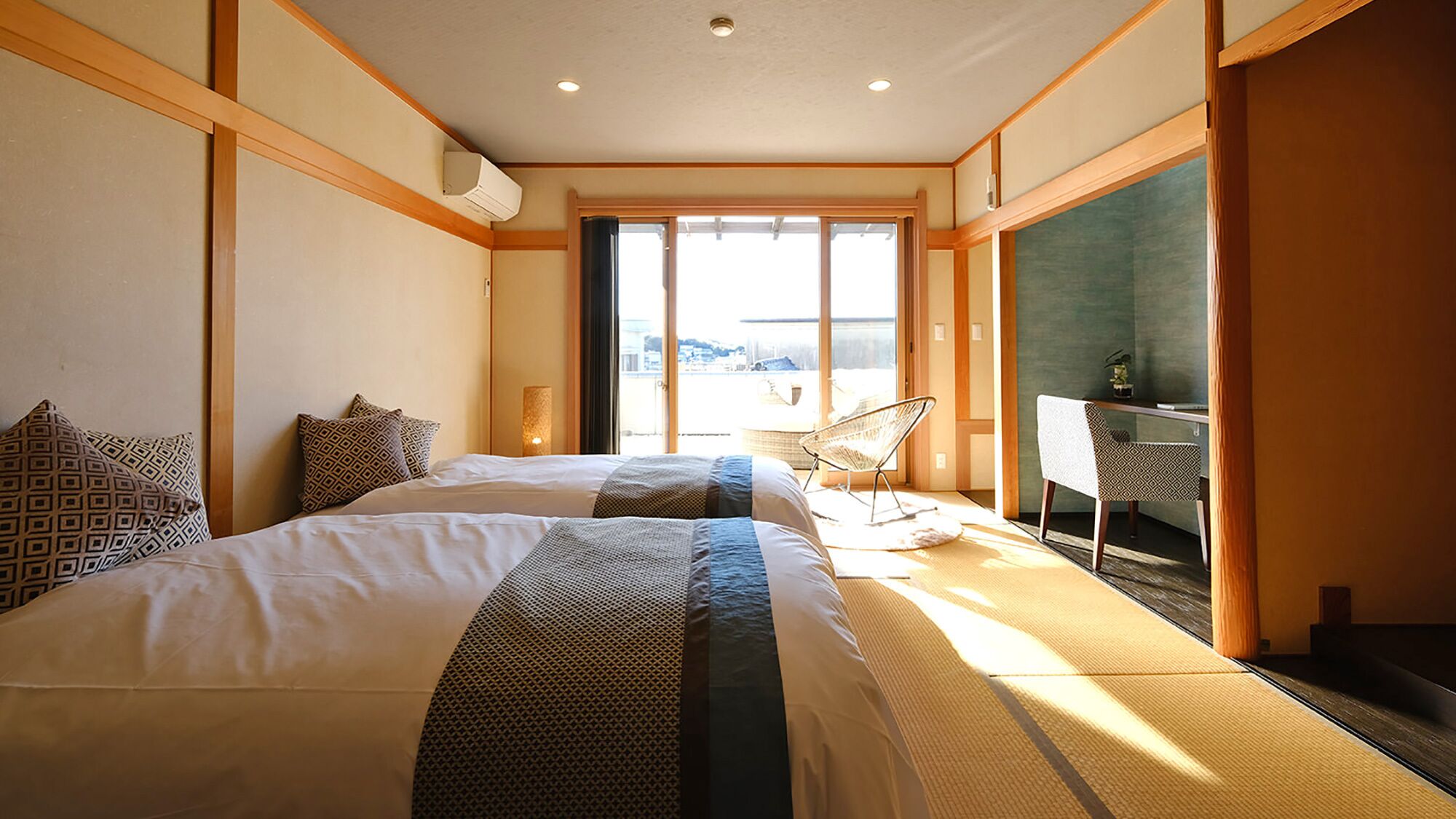 Quarto de hotel com duas camas, uma escrivaninha, uma cadeira e uma janela grande.