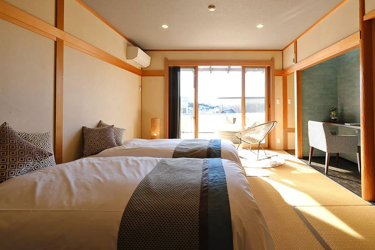 A hotel room with two beds, a desk, a chair, and a large window.