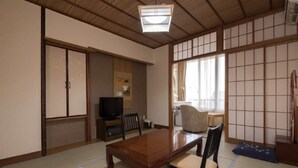 A traditional Japanese room with tatami flooring, a low wooden table, and a television in the background. - Izu Nagaoka Onsen Kkr Izu Nagaoka Chitoseso (Izunokuni)