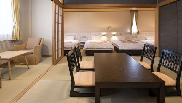 A traditional Japanese-style room with tatami flooring, a low table with chairs, and a futon bed arrangement. - Izu Nagaoka Onsen Kkr Izu Nagaoka Chitoseso (Izunokuni)