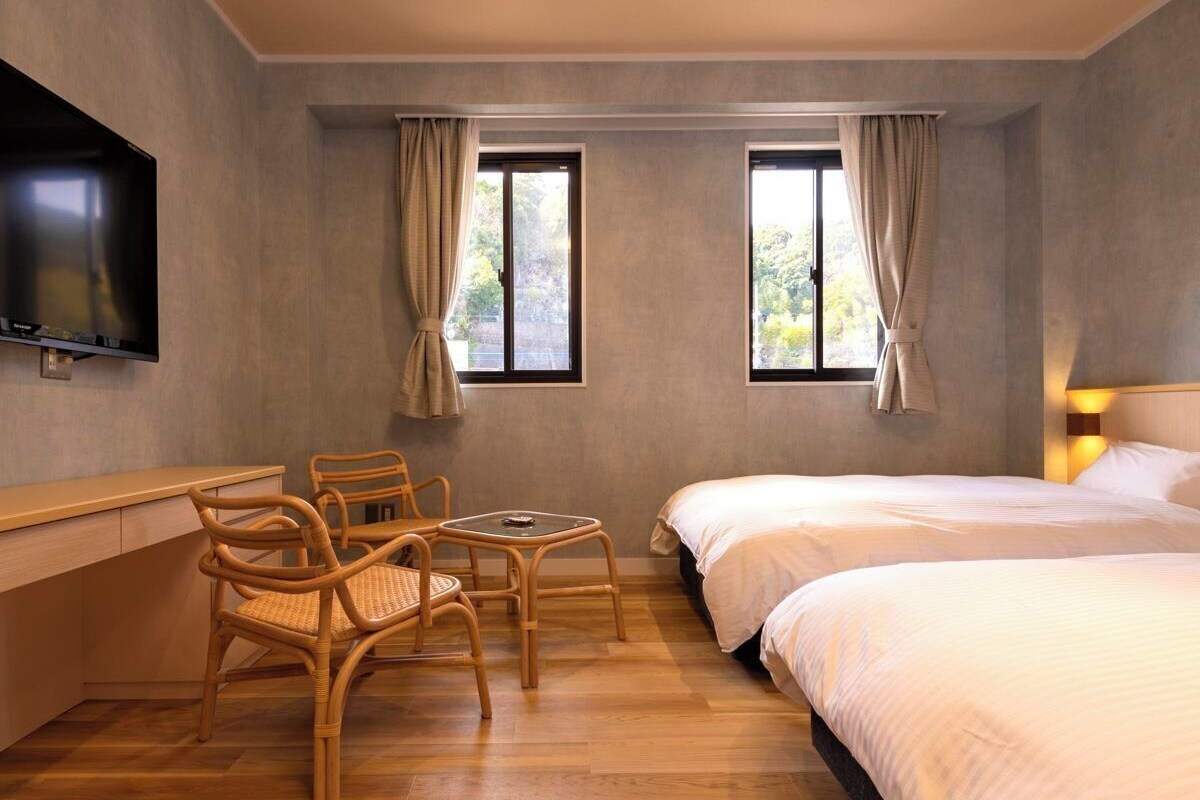 A hotel room with a bed, a desk, a chair, and a TV.