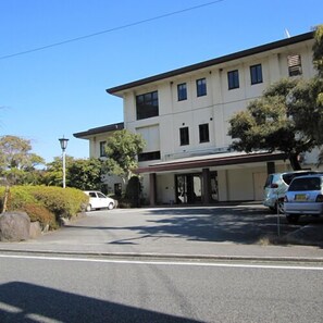 A two-story building with a flat roof, a covered entrance, and a parking area with cars. - Izu Nagaoka Onsen Kkr Izu Nagaoka Chitoseso (Izunokuni)