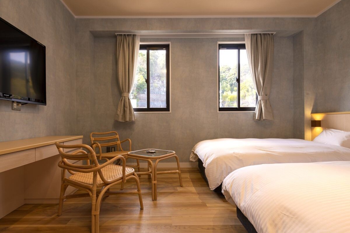 A hotel room with a bed, a desk, two chairs, and a TV.