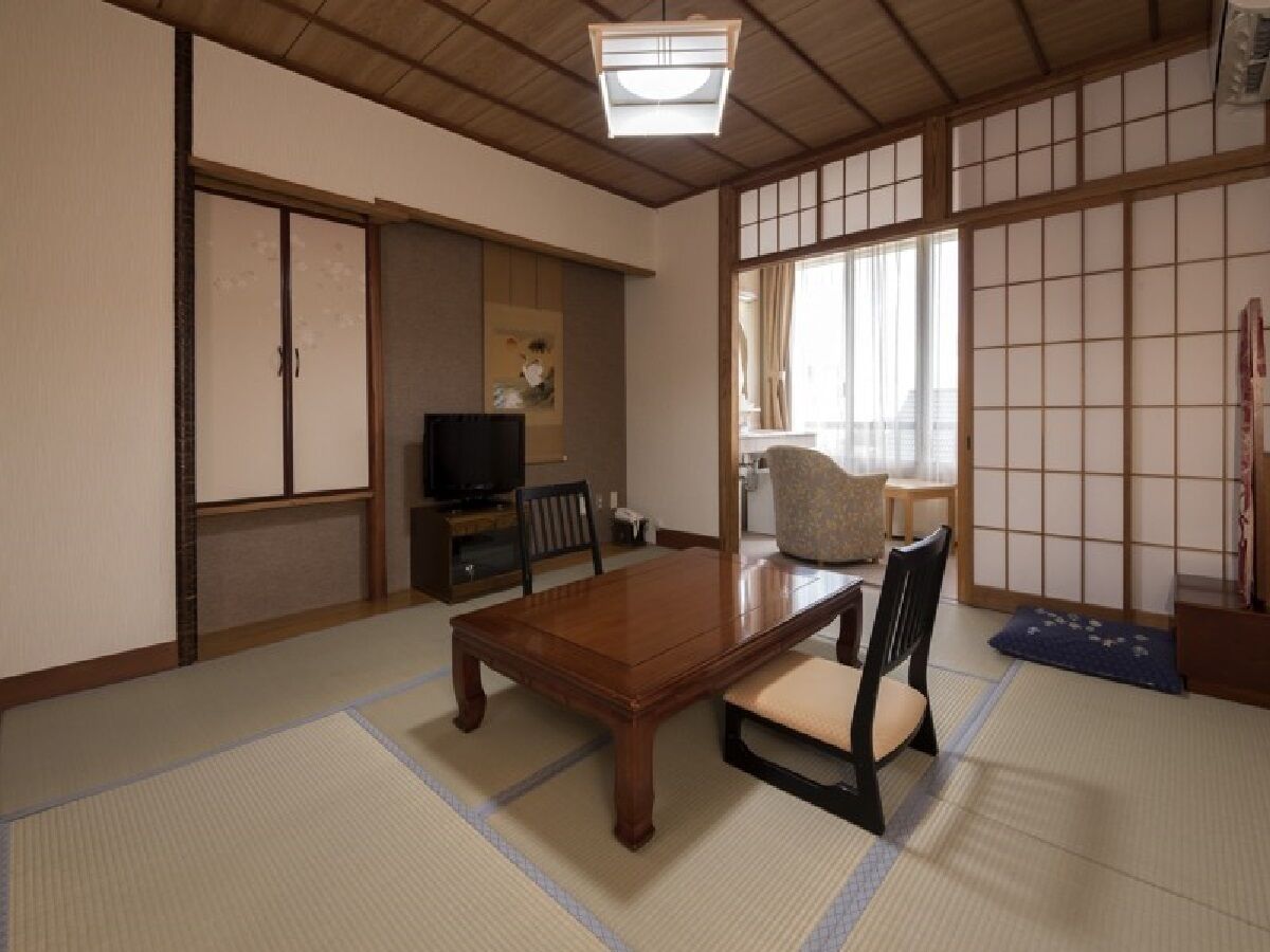 A traditional Japanese room with tatami flooring, a low wooden table, and a television.