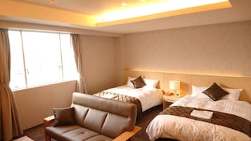 Quarto de hotel com duas camas, um sofá, uma mesa de cabeceira com luminária e uma janela com cortinas.