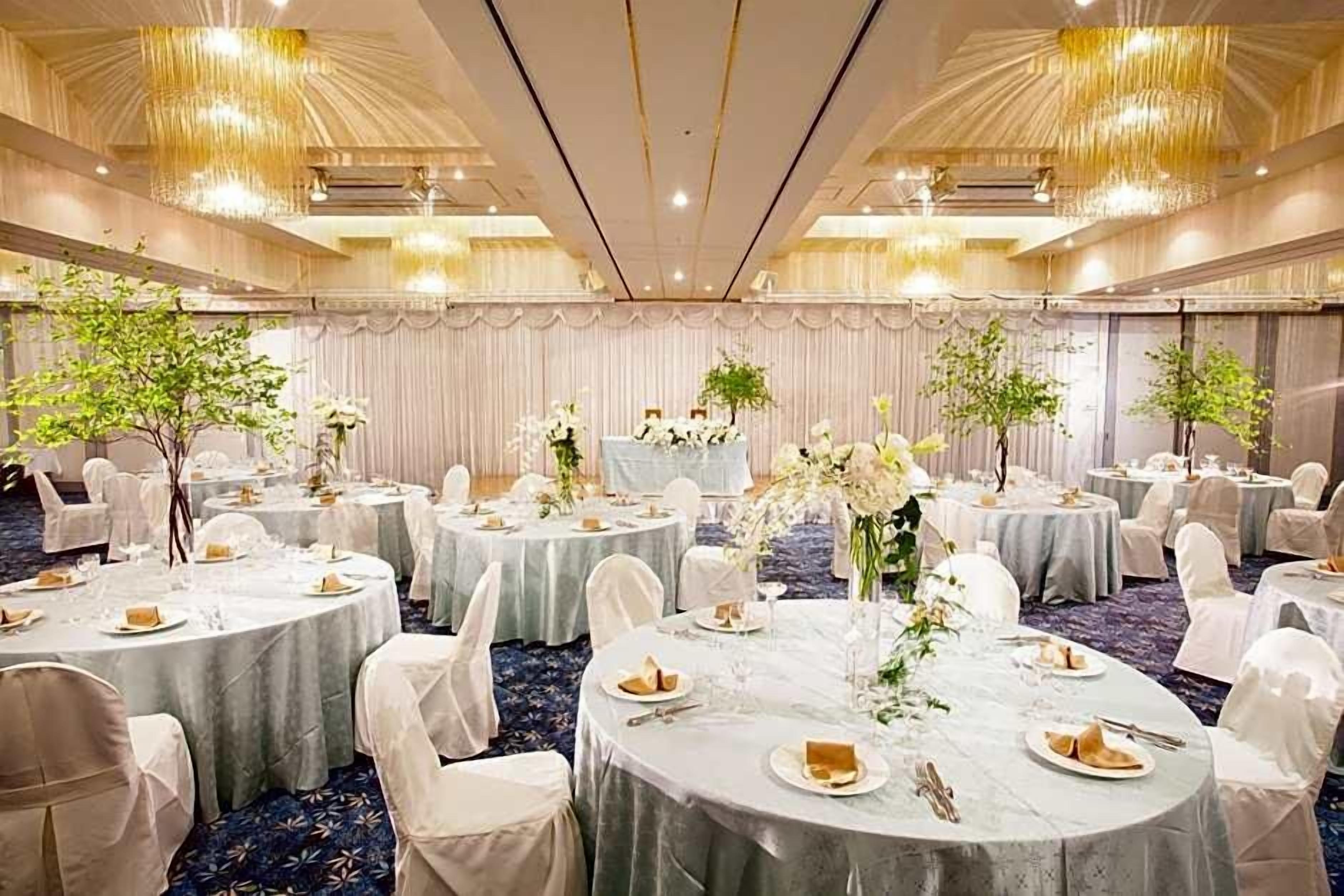 A banquet hall with round tables, white chairs, and floral centerpieces.