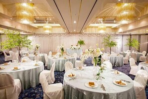 A banquet hall with round tables, white chairs, and floral centerpieces.
