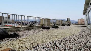 A rooftop terrace with a gravel surface, a metal railing, and a view of the cityscape.
