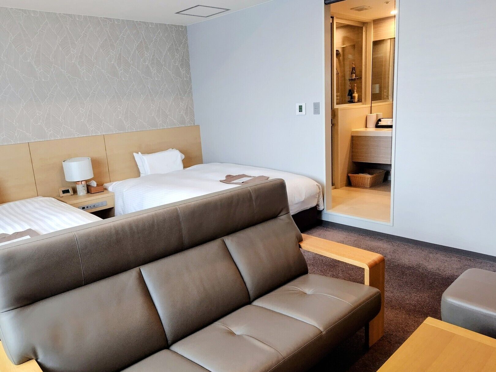 A hotel room with a bed, a sofa, a nightstand, and a bathroom visible through an open door.