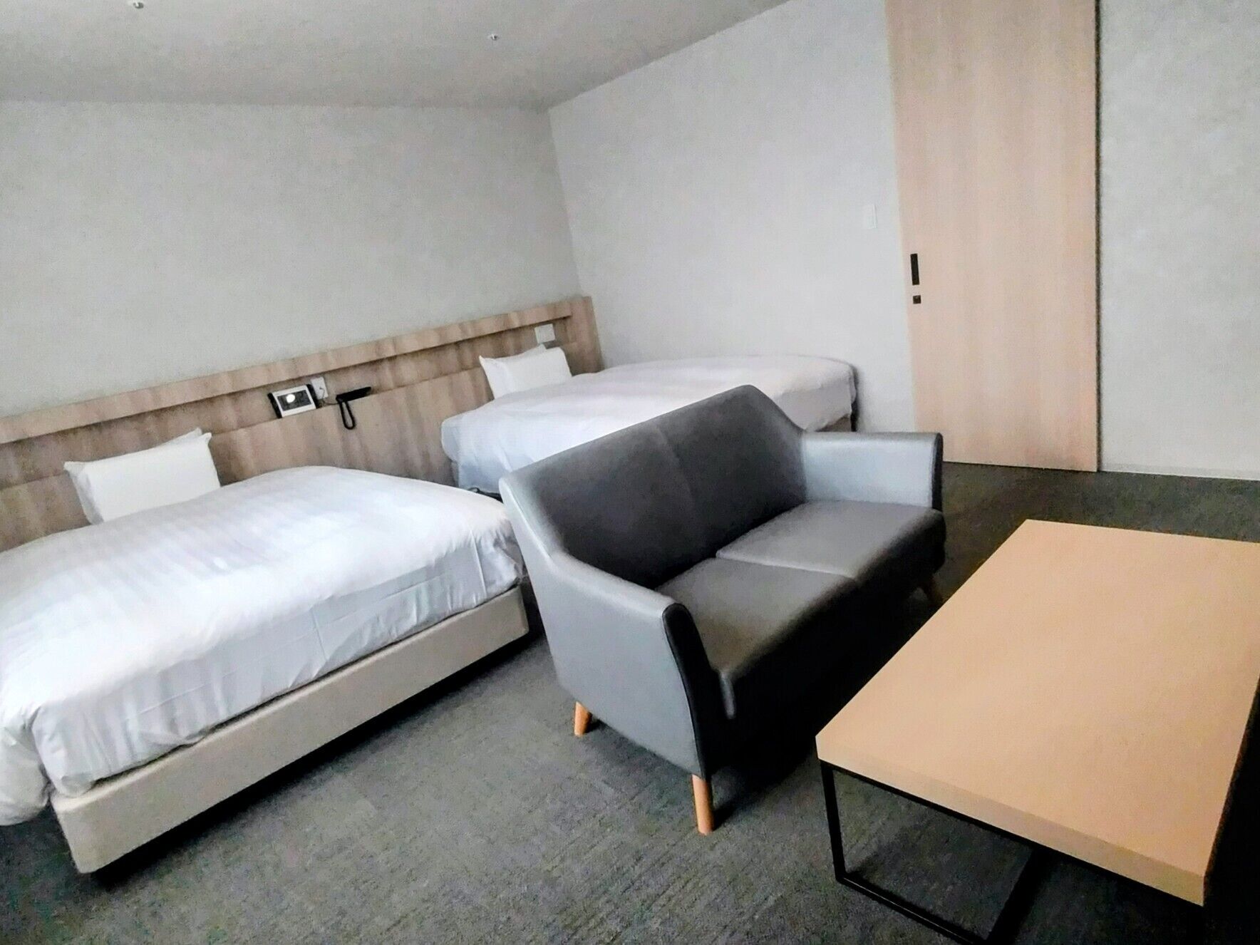 A hotel room with two single beds, a grey sofa, and a small table.