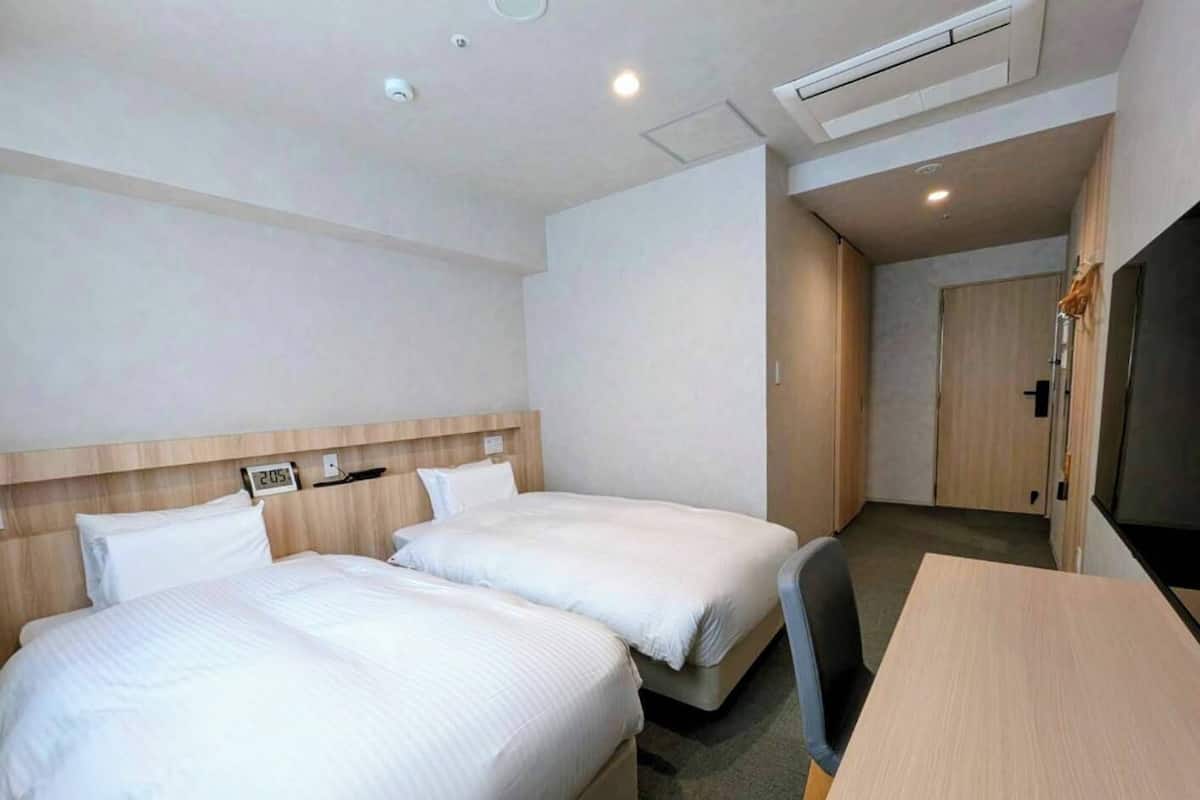 A hotel room with two beds, a desk, and a wardrobe.