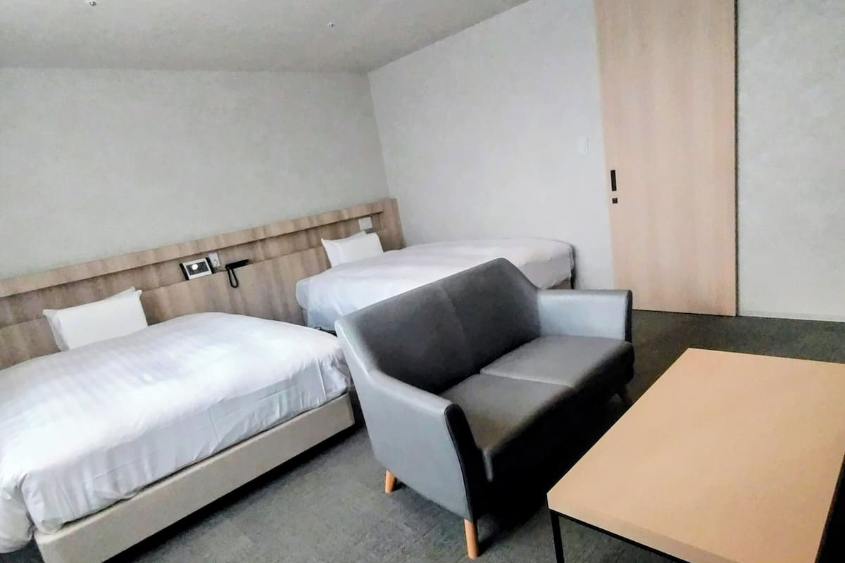 A hotel room with two beds, a sofa, and a small table.