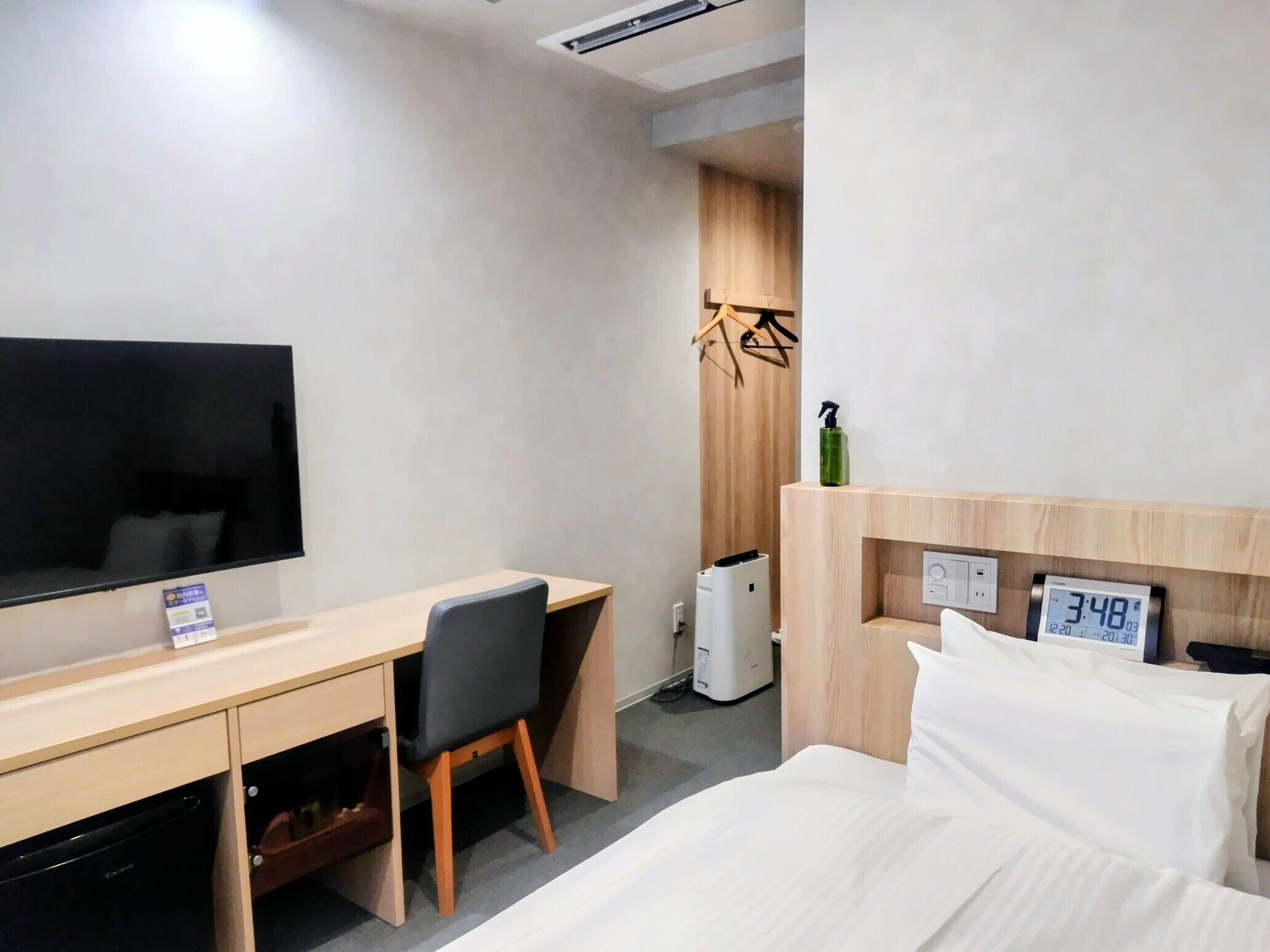 A hotel room with a bed, a desk with a chair, a television, a heater, and a clock.